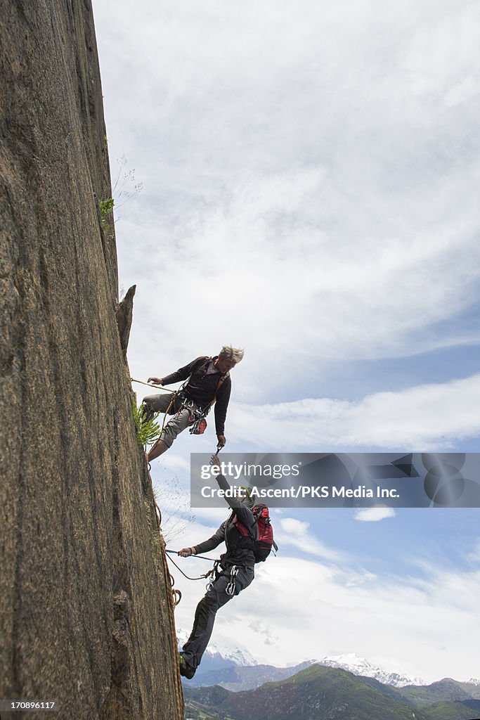 Climber passes gear along to partner, on rock face