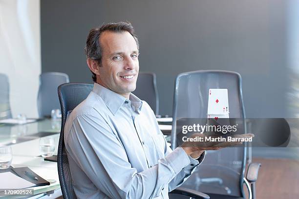 businessman holding house of cards in conference room - card house stock pictures, royalty-free photos & images