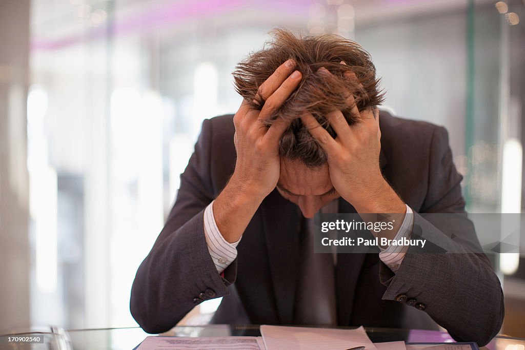 Frustriert Geschäftsmann sitzt am Schreibtisch mit Kopf in den Händen