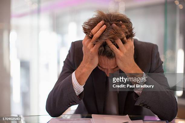 frustrado ejecutivo sentado en el escritorio con la cabeza en las manos - frustración fotografías e imágenes de stock