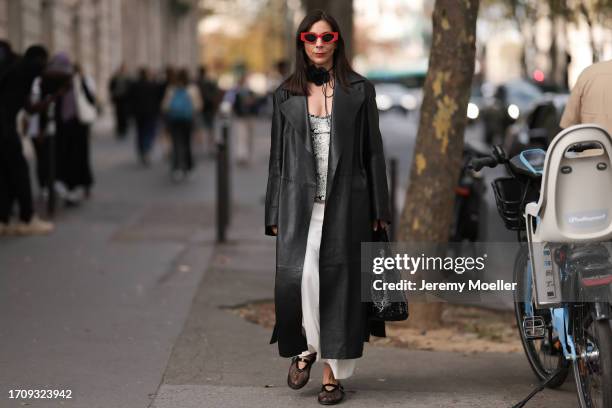 Daniela Lipps is seen outside Gauchere show wearing red sunnies, flower neck detail, long black leather coat, snake print shirt, black sequin tote...