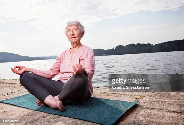 senior woman practising yoga at lake - senior essen stockfoto's en -beelden