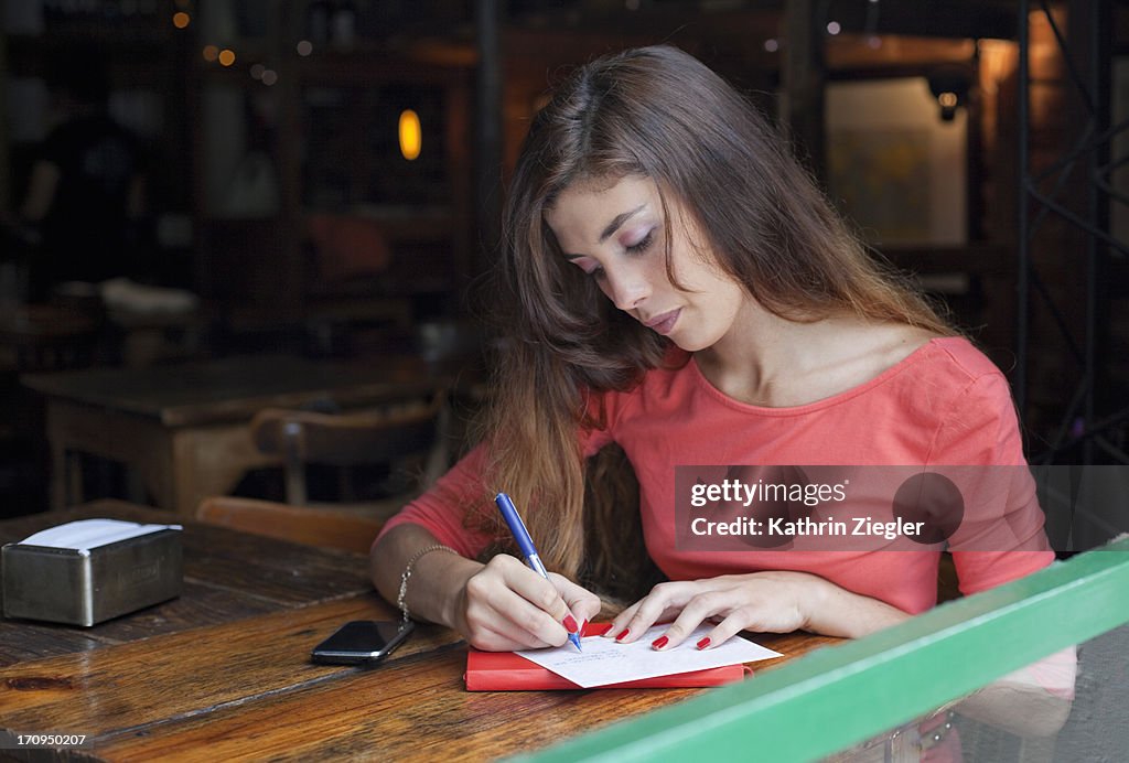 Young woman writing postcards at a café