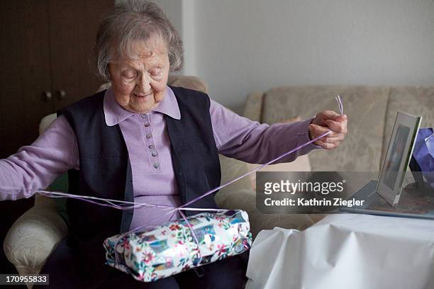 senior woman unwrapping birthday presents - present unwrap stock-fotos und bilder
