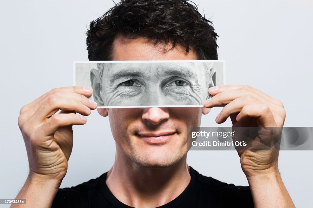 Young man holding picture of old eyes over his