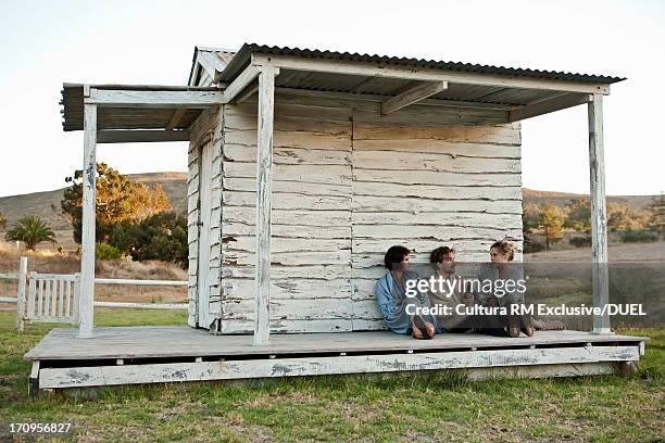 three friends sitting outside beach hut wrapped in blankets - strandhütte stock-fotos und bilder