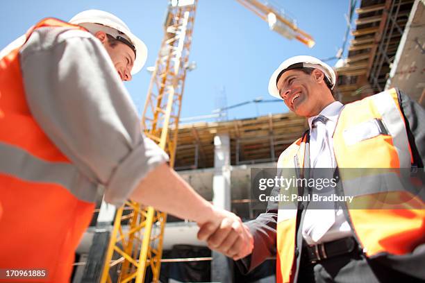 construction workers shaking hands on construction site - low angle view of two businessmen standing face to face outdoors stock pictures, royalty-free photos & images