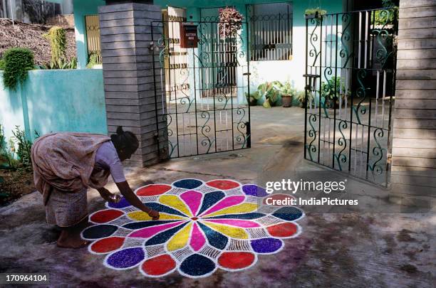 Woman celebrating the festival of Pongal by making a rangoli in the courtyard of her home, Kochi, Kerala, India.