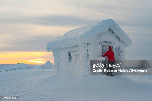 hiker watching sunset from a snowy mountain hut - van de gebaande paden stockfoto's en -beelden