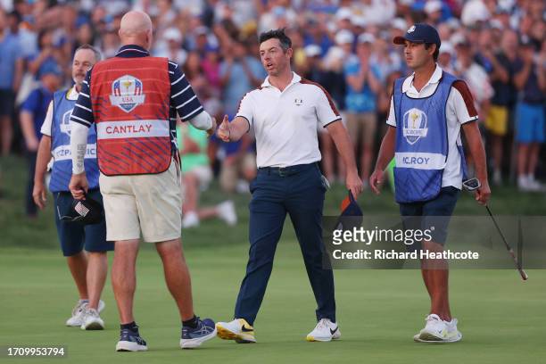 Rory McIlroy of Team Europe shakes hands with caddie of Patrick Cantlay of Team United States Joe LaCava on the 18th green during the Saturday...