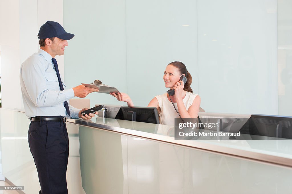 Delivery man handing notepad to receptionist