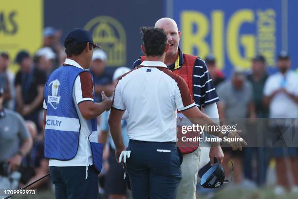 Rory McIlroy of Team Europe interacts with caddie of Patrick Cantlay of Team United States, Joe LaCava on the 18th green during the Saturday...