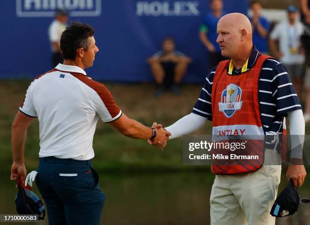 Rory McIlroy of Team Europe shakes hands with caddie of Patrick Cantlay of Team United States Joe LaCava on the 18th green during the Saturday...