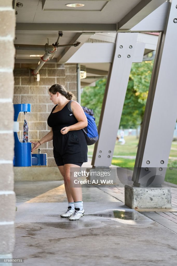 Woman football player filling bottle with water from cooler