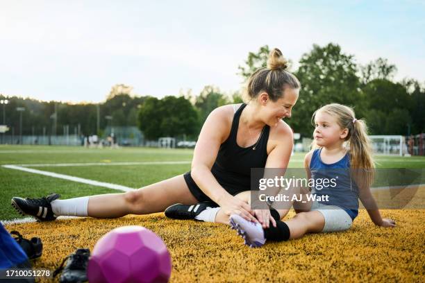 mother tying shoelaces of a daughter sitting on soccer field for practice - parents sideline stock pictures, royalty-free photos & images