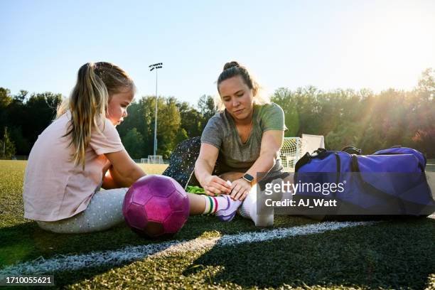 mother soccer player tying shoe lace of daughter on field for practice - parents sideline stock pictures, royalty-free photos & images