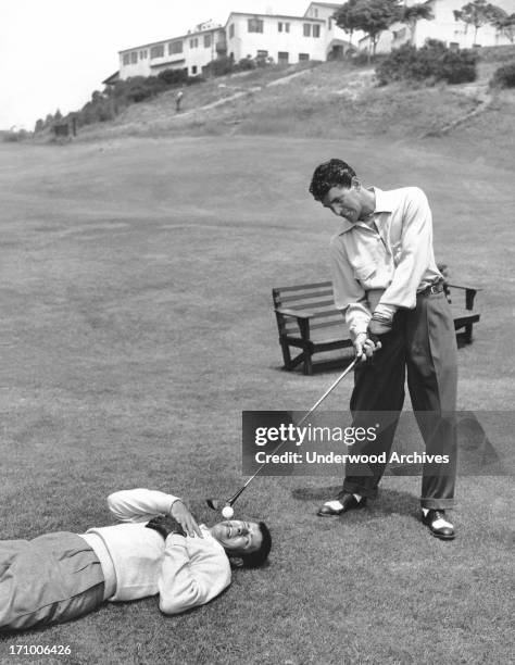 Dean Martin appears to be ready to drive off a tee that Jerry Lewis is fearfully holding in his mouth, California, 1953.