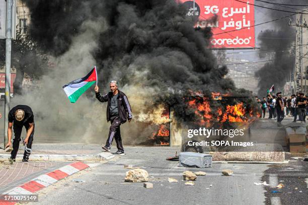 Palestinian protesters burn containers and tires and block streets during a demonstration after Jewish settlers attacked them and killed a...