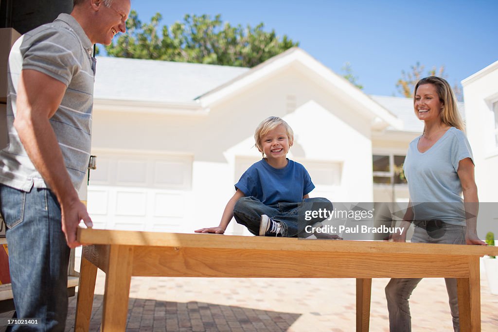 Parents and son moving table from moving van into house