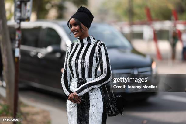 Halima Aden is seen outside Nina Ricci show wearing black head piece, black and white striped sequin long dress, silver studded handbag and black...