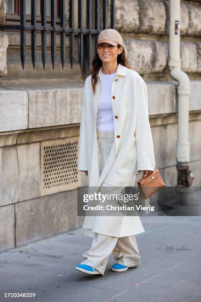 Deborah Reyner Sebag wears brown cap, creme white coat, pants, white shirt outside Hermes during the Womenswear Spring/Summer 2024 as part of Paris...