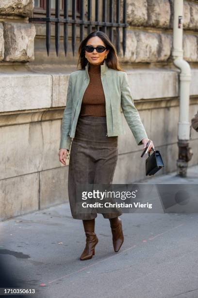 Guest wears brown turtleneck, green jacket, wild leather skirt, black bag, brown boots outside Hermes during the Womenswear Spring/Summer 2024 as...