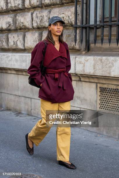 Guest wears cap, burgundy jacket, beige pants with side pockets outside Hermes during the Womenswear Spring/Summer 2024 as part of Paris Fashion Week...
