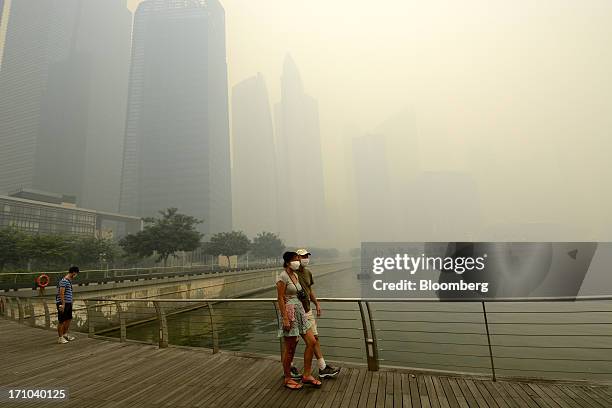 Couple wearing face masks walk along the boardwalk at Marina Bay as buildings in the central business district stand shrouded in smog in Singapore,...