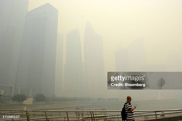 Man looks out towards the city skyline from the boardwalk at Marina Bay as buildings in the central business district stand shrouded in smog in...