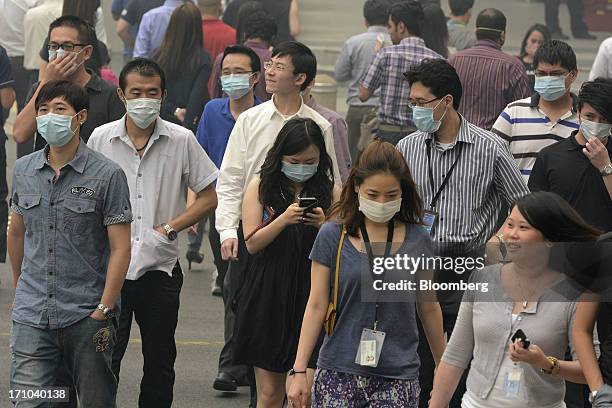 Pedestrians and office workers wear face masks as they cross a street in Singapore, on Friday, June 21, 2013. Singapore's smog hit its worst level,...