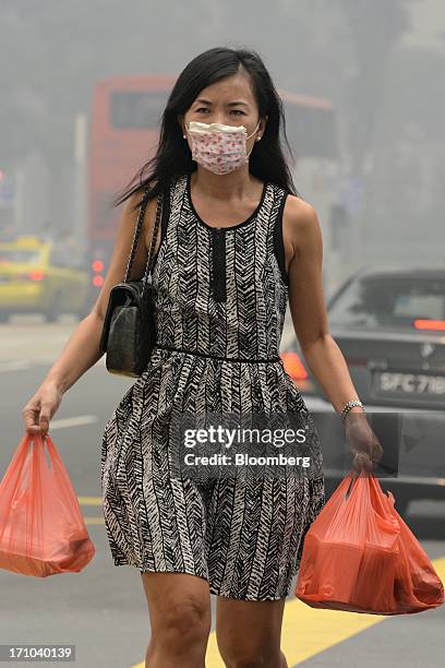 Woman wearing a face mask carries bags of takeaway food as she walks along a road during lunch hour in Singapore, on Friday, June 21, 2013....