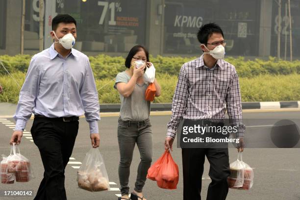 Office workers wearing face masks carry bags of takeaway food as they cross a road during lunch hour in Singapore, on Friday, June 21, 2013....