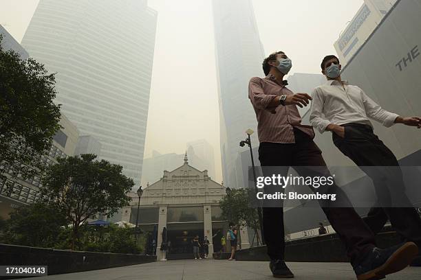 Office workers wearing face masks walk through Raffles Place as office buildings stand shrouded in smog in Singapore, on Friday, June 21, 2013....