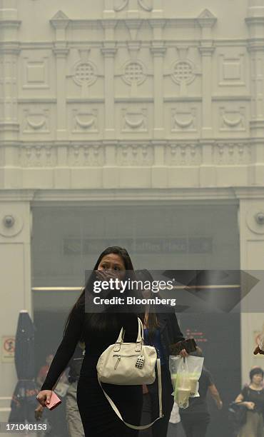 Woman covers her mouth and nose as she walks through Raffles Place in Singapore, on Friday, June 21, 2013. Singapore's smog hit its worst level,...