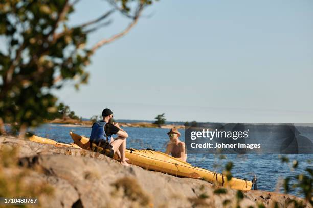 men sitting near kayaks at rocky coast - kayaking stockholm stock pictures, royalty-free photos & images