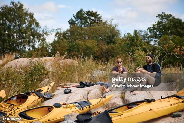 men sitting at rocks on coast near kayaks - stockholm summer stock-fotos und bilder