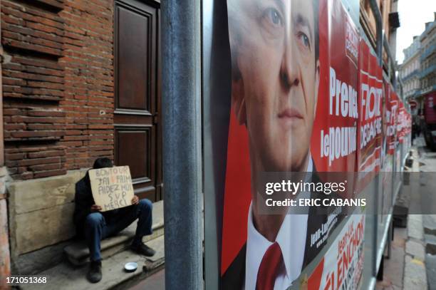 Man begs for money next to a campaign poster of French Front de Gauche leftist candidate for the 2012 French presidential election Jean-Luc Melenchon...