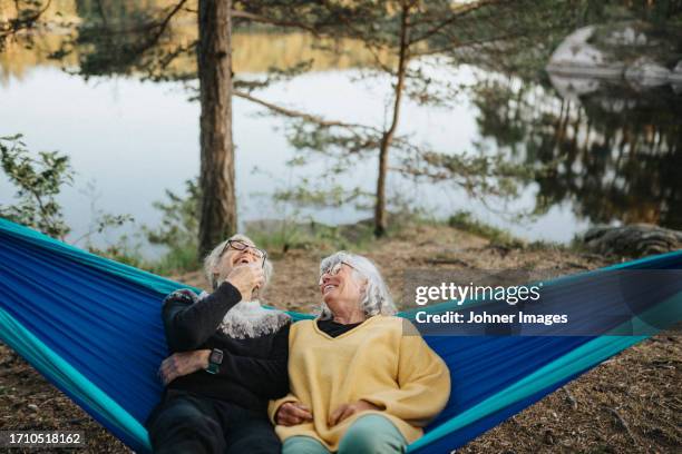 two senior women resting in hammock at lakeshore - mujeres mayores fotografías e imágenes de stock