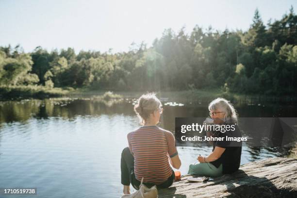 two senior women sitting on rock at lakeshore - svensk sommar bildbanksfoton och bilder