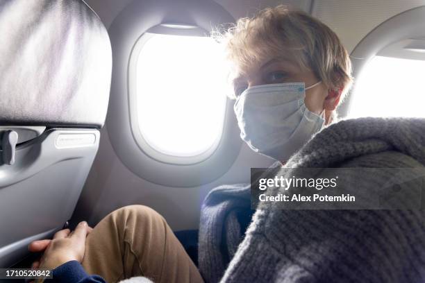 travelling during pandemic. mature blond women, sitting in airplane, looking at camera. - alex potemkin coronavirus stock pictures, royalty-free photos & images