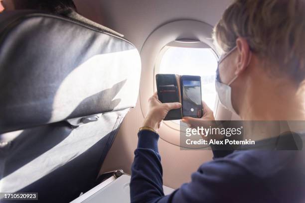 making video from airplane window. mature women making video from the window during the flight. - alex potemkin coronavirus stock pictures, royalty-free photos & images