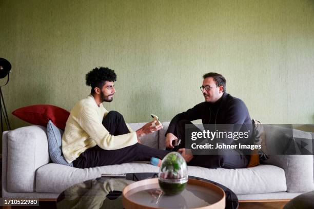 gay couple relaxing on sofa at home and using phones - phone couple stock pictures, royalty-free photos & images
