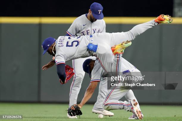 Adolis Garcia of the Texas Rangers falls over Leody Taveras as Marcus Semien looks on as they are unable to come up with a catch on a single hit by...