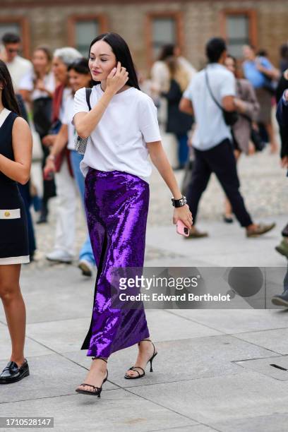 Guest wears a studded bangle, a white top, a sparkling purple sequined long skirt, black high heeled sandals , outside Alberta Ferretti, during the...