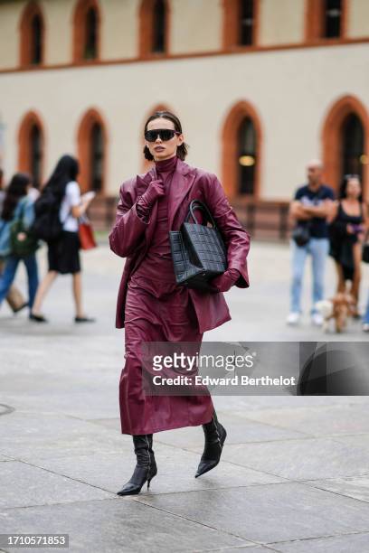 Guest wears sunglasses, a raspberry color leather hi-neck top, a matching oversized jacket, matching gloves, matching maxi skirt, black leather...