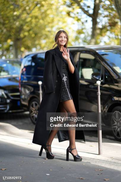Lorena Rae wears a long black coat, a black mini / short tweed checked dress, tights, platform high heels shoes, outside Elie Saab, during the...