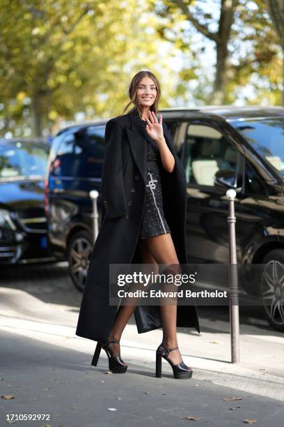 Lorena Rae wears a long black coat, a black mini / short tweed checked dress, tights, platform high heels shoes, outside Elie Saab, during the...