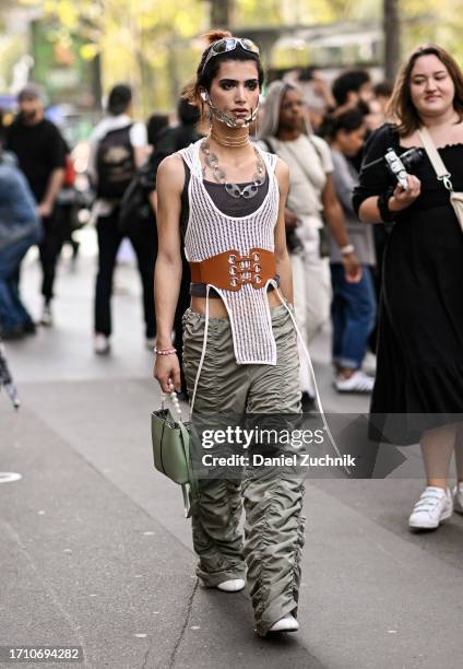 Guest is seen wearing a knit top, gray top, brown belt, green ruffled pants, green bag and silver headpiece and necklace outside the Hermes show...