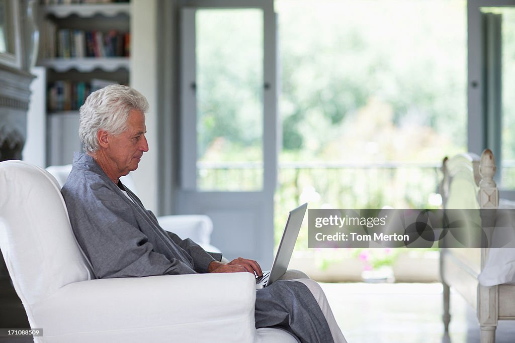 Senior man in bathrobe using laptop in bedroom