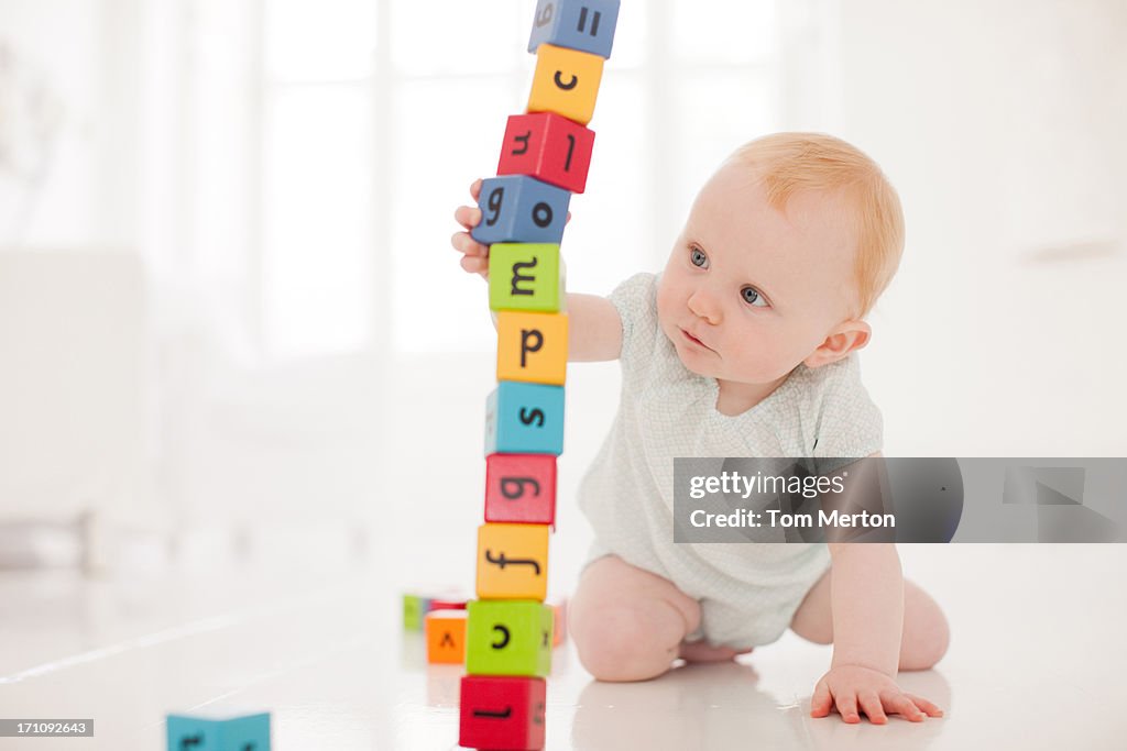 Baby on floor pulling wood block from middle of stack